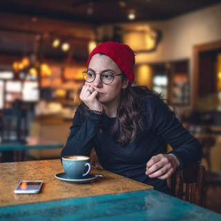 Eine junge Frau sitzt alleine am Tisch, ihr Smartphone liegt vor ihr.