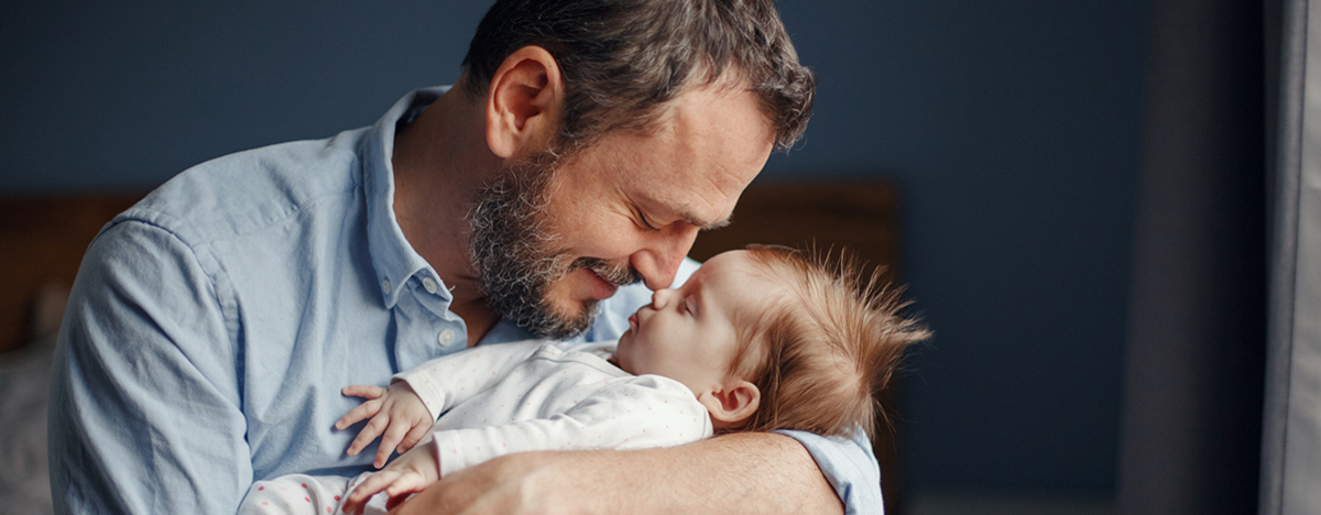 Vater im mittleren Alter küsst schlafendes neugeborenes Mädchen