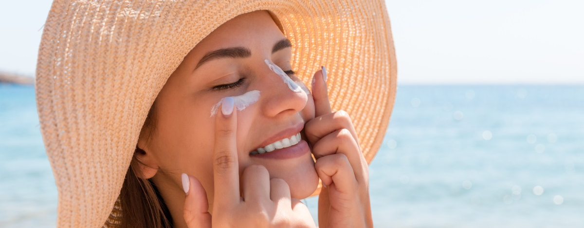 Nahaufnahme einer Frau am Strand, die sich Sonnencreme ins Gesicht schmiert