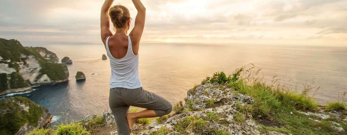 Frau steht auf einer Klippe und macht eine Yoga-Übung