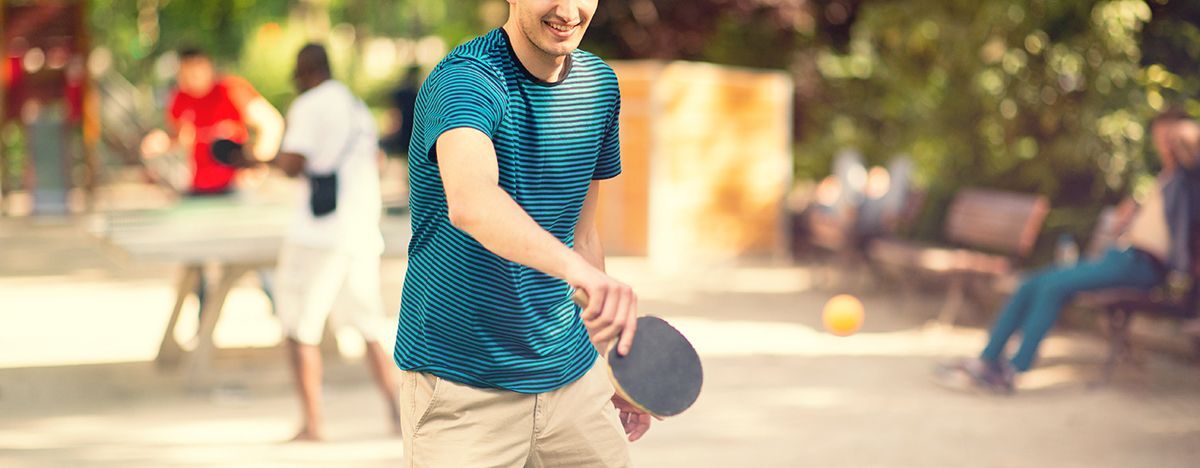 Junger Mann spielt draußen Tischtennis an einer Tischtennisplatte