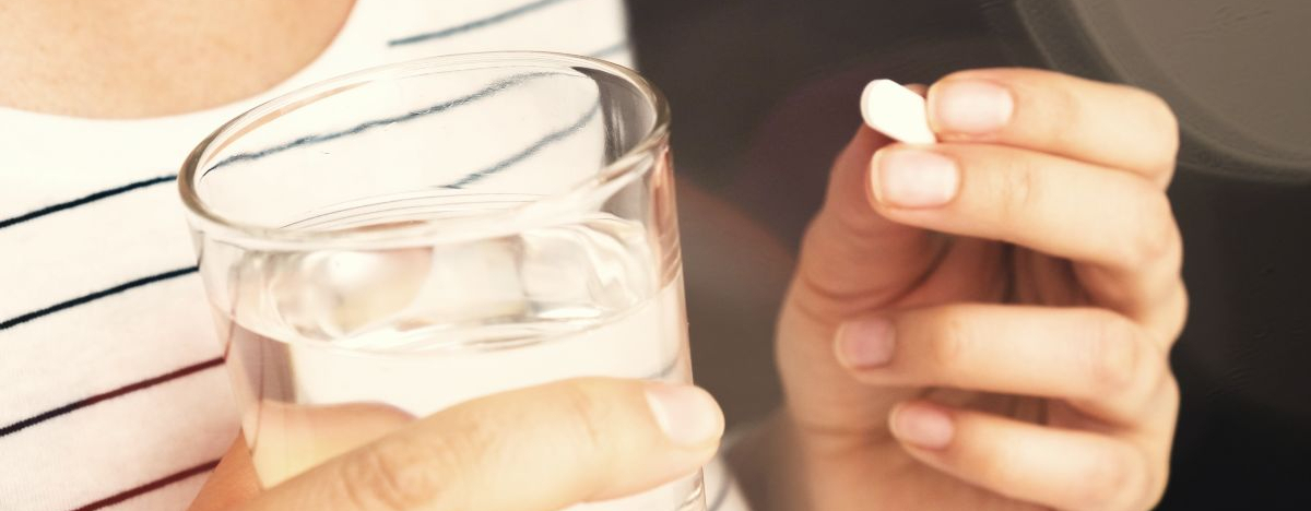 Eine Frau hält ein Glas mit Wasser und eine Tablette in den Händen