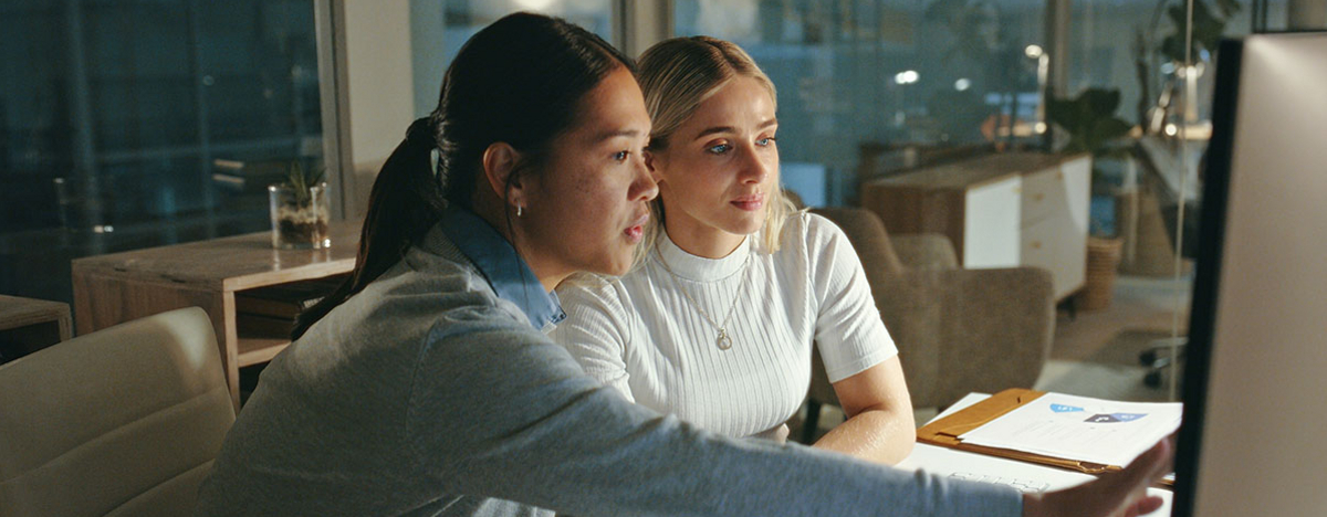 Zwei Frauen, die zusammen über ein Projekt vor einem Computer sprechen