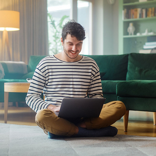 Mann mit Laptop, während er auf dem Wohnzimmerboden sitzt