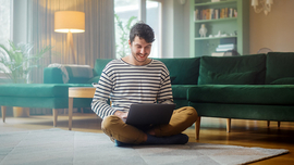 Mann mit Laptop, während er auf dem Wohnzimmerboden sitzt