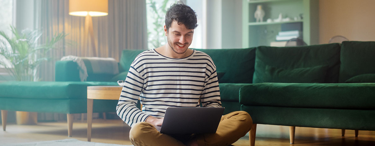 Mann mit Laptop, während er auf dem Wohnzimmerboden sitzt