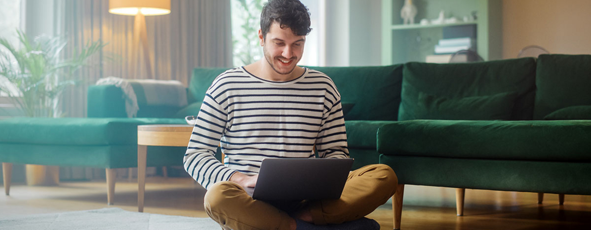 Mann mit Laptop, während er auf dem Wohnzimmerboden sitzt