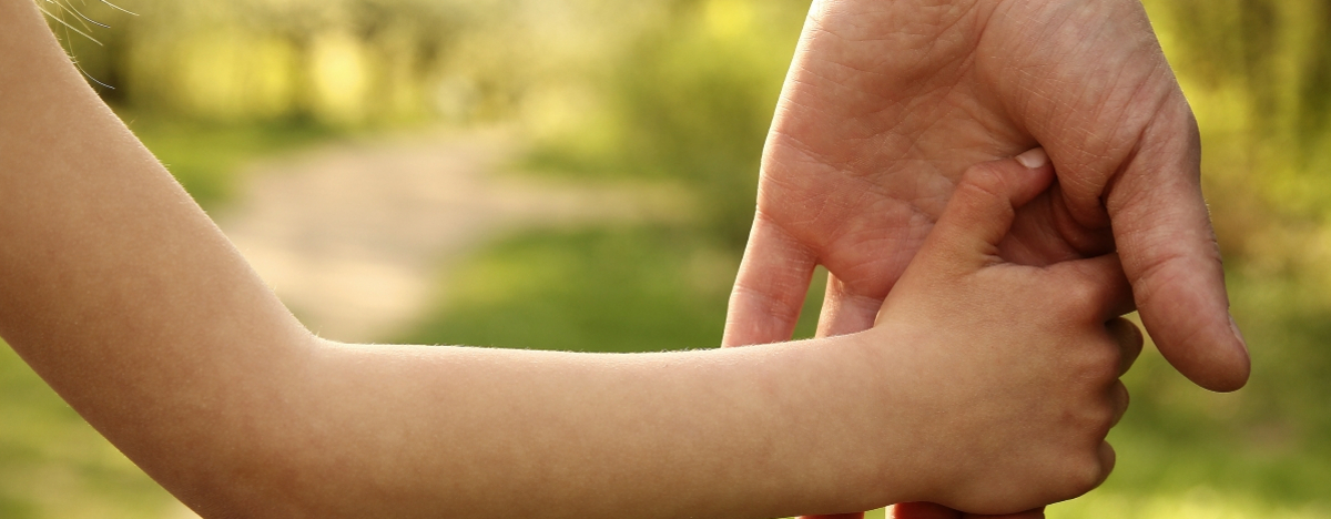 Eine Kinderhand hält sich an einer Hand eines Erwachsenden fest.