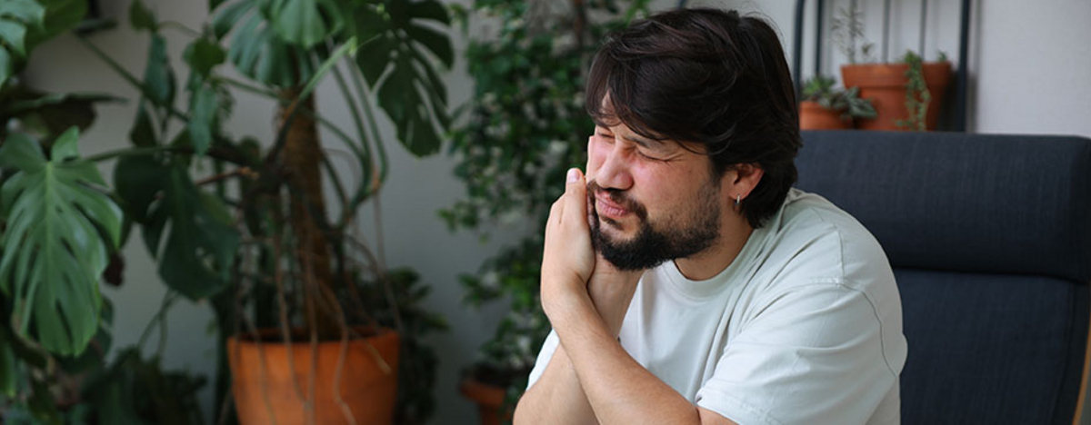 Junger Mann fasst sich ins Gesicht vor Schmerzen