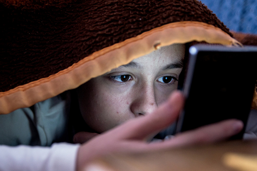 Mädchen im Bett starrt auf ihr Smartphone