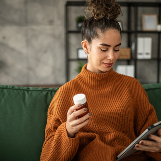 Junge Frau nimmt Medizin und recherchiert die Nebenwirkungen auf ihrem Tablet.