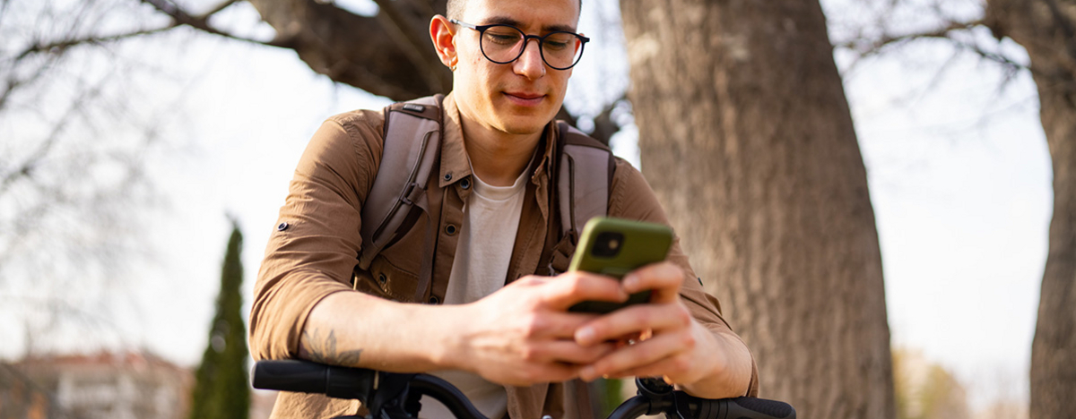 Junger Mann benutzt Handy und steht neben seinem Fahrrad draußen.