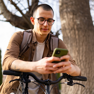 Junger Mann benutzt Handy und steht neben seinem Fahrrad draußen.