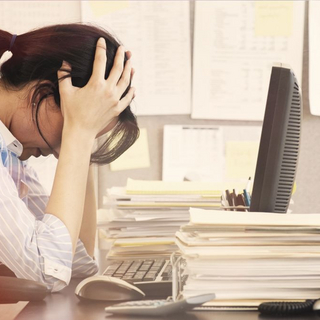 Frau im Büro schlägt vor lauter Stress die Arme über dem Kopf zusammen