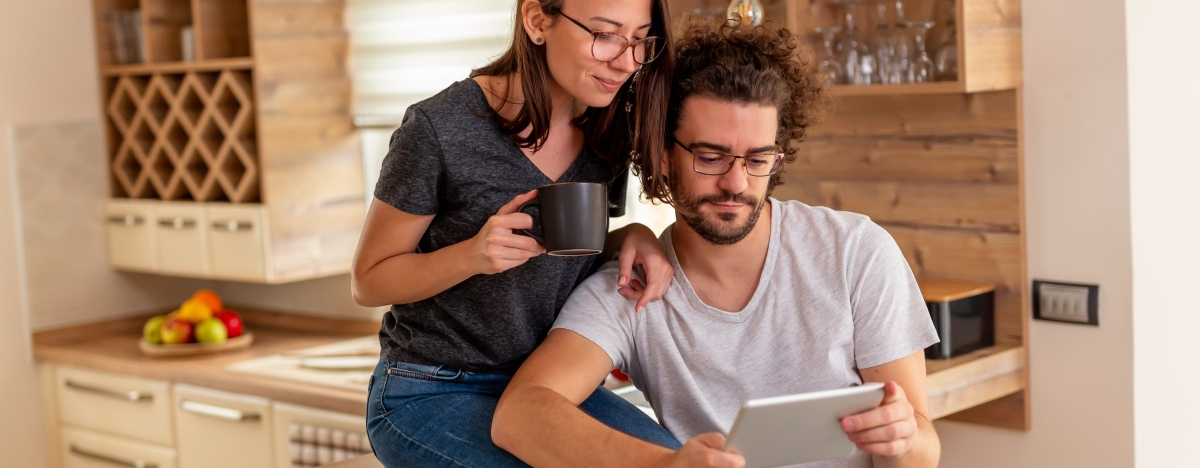 Eine Frau und ein Mann lesen zusammen etwas auf einem Tablet-Computer in der Küche