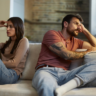 Ein frustriertes Paar sitzt auf der Couch, schaut in unterschiedliche Richtungen.