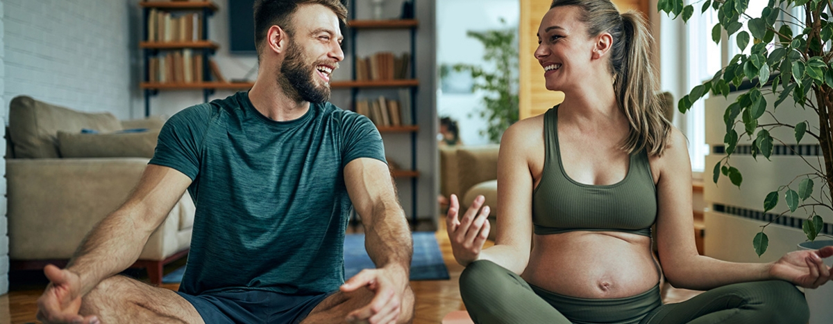 Schwangere junge Frau, die mit ihrem Mann zu Hause Yoga praktiziert