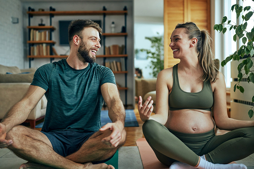 Schwangere junge Frau, die mit ihrem Mann zu Hause Yoga praktiziert