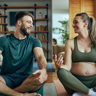 Schwangere junge Frau, die mit ihrem Mann zu Hause Yoga praktiziert