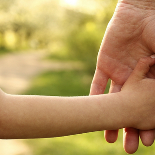 Eine Kinderhand hält sich an einer Hand eines Erwachsenden fest.