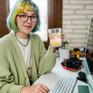 Eine junge Frau sitzt am Computer und trinkt Zitronenwasser.