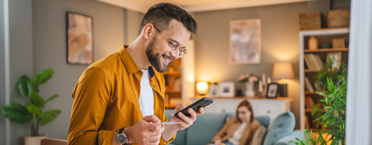 Junger Mann schaut auf sein Handy und hält seine Gesundheitskarte in der Hand