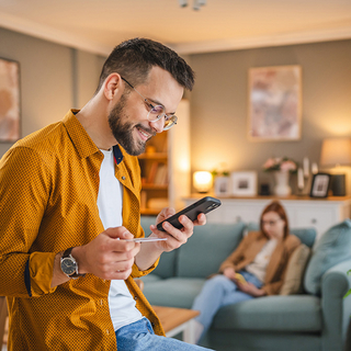 Junger Mann schaut auf sein Handy und hält seine Gesundheitskarte in der Hand