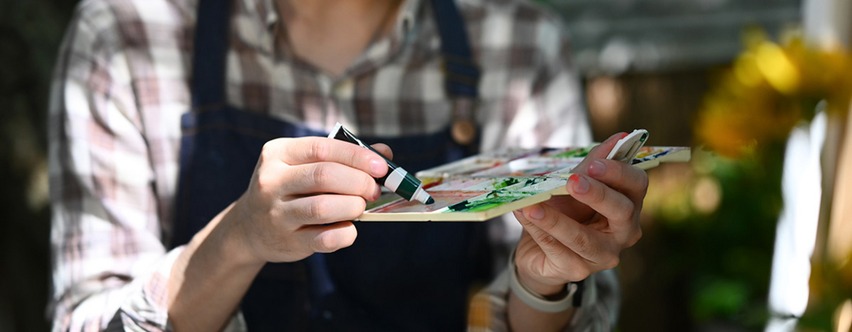 Künstler in Schürze mischt Farben auf Palette für sein neues Projekt