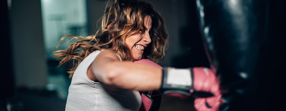 Eine Frau mit Boxhandschuhen, die alleine im Fitnessstudio einen Boxsack boxt.