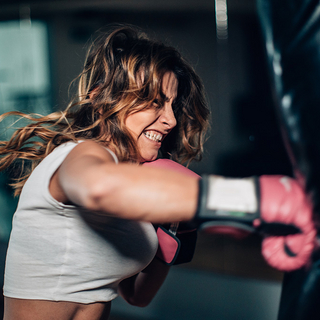 Eine Frau mit Boxhandschuhen, die alleine im Fitnessstudio einen Boxsack boxt.