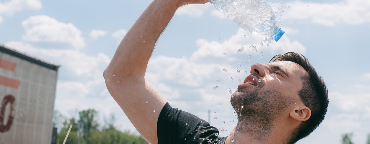 Mann schüttet sich Wasser aus einer Plastikflasche über den Kopf