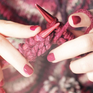 Frau strickt mit roter Wolle.