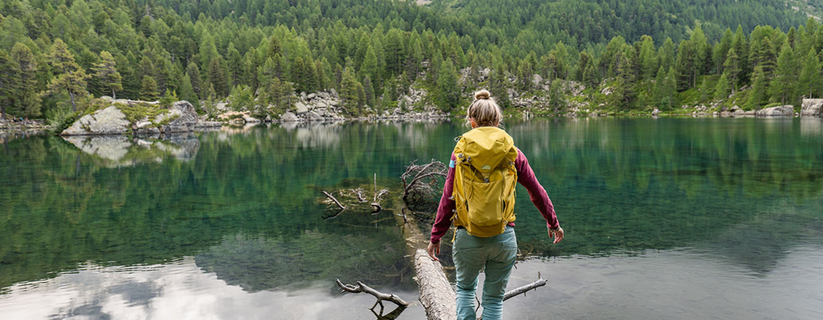 Frau geht über einen Baumstamm an einem See