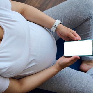 schwangere Frau sitzt auf einer yoga-Mappe und schaut auf ihr Handy