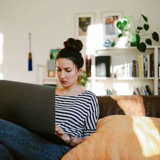 Junge Frau, die von Zuhause aus am Laptop arbeitet