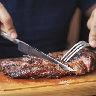 Ein Stück Fleisch liegt auf einem Brett und wird mit Messer und Gabel geschnitten.