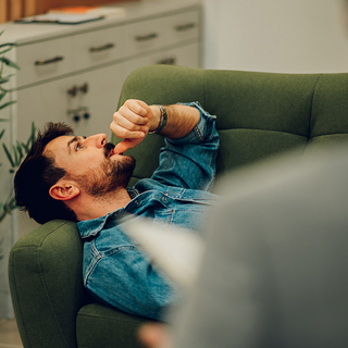 Ein depressiver Mann liegt auf einem Sofa in der Praxis eines Psychotherapeuten.