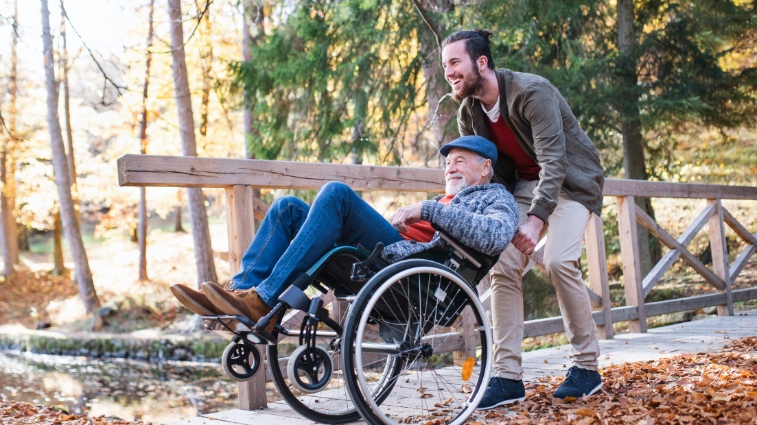 Junger Mann schiebt Senior im Rollstuhl