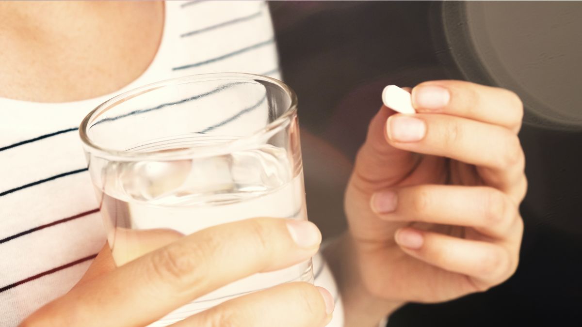 Eine Frau hält ein Glas mit Wasser und eine Tablette in den Händen
